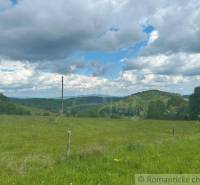 The landscape in České Brezovy with green gardens, hills, and a cloudy sky.