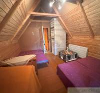 Attic room in a cabin with a slanted wooden ceiling, two beds, and a table.