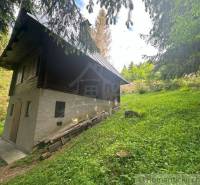 A cottage in Kokava nad Rimavicou surrounded by coniferous and deciduous trees, on a gentle slope.