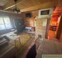 A wooden interior of a cabin with a tiled stove and a living area.