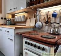 A kitchen in a cottage with wooden details, an old stove, and hanging utensils.
