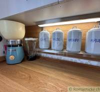 The kitchen shelf of the cottage with jars for sugar, rice, groats, semolina, and a grinder.
