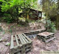 A wooden cabin in Bratislava - Lamač surrounded by pallet furniture and forest vegetation.