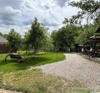 The garden of the cottage in Bratislava-Lamač with benches, trees, and a gravel path.