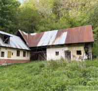 An older family house in Hačava, surrounded by greenery and trees, with rusty roofs.