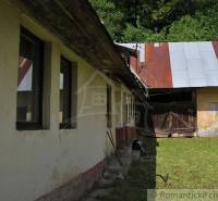 A family house in Hačava with a garden, a wooden fence, and a metal roof surrounded by nature.
