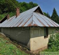 A family house in Hačava with a metal roof, situated near a forest and a green meadow.
