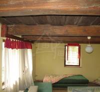 Interior of a family house with a wooden ceiling, bed, and curtains.