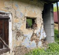 A weathered wall of a family house in Hačava with wooden doors and damaged plaster.