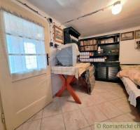 The interior of a cottage with cream-colored doors, a table, and a sofa, a shelf with books and decorations.