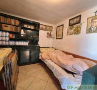 A room in a cottage with a bed, a bookshelf, and paintings on the wall.