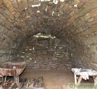 Stone vaulted cellar space with a wheelbarrow and wooden pallets in the gardens.