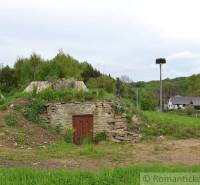 Stone cellar with a green roof in the Gardens in Kečkovce and rural houses in the background.