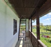 A wooden terrace with stairs at the cottage in Podkriváň offers a view of the surrounding countryside.