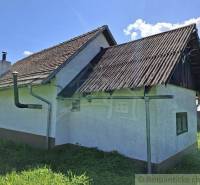 A cottage in Podkriváni with a tin roof and green surroundings under a blue sky.