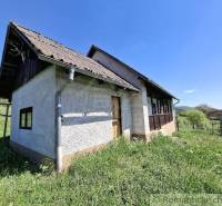 A cottage in Podkriváni with a wooden roof, surrounded by grass and a wooden fence.