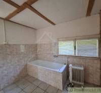 A bathroom in a cabin with a bathtub and a radiator, tiled with a view from the window.
