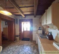 A kitchen in a cottage with a wooden ceiling and stone floor, warm lighting.