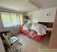 A room in a family house with a bed, a chair, and cracks on the wall.