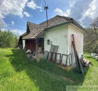 A family house in Kokava nad Rimavicou surrounded by grass and trees, with partially worn-off plaster.