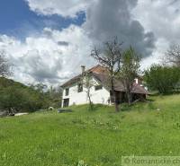 A family house in Kokava nad Rimavicou surrounded by greenery and old trees under a sky with clouds.