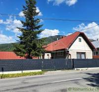A family house in Telgárt with a red roof, a tall tree, a fence, and a road.