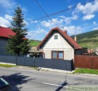 A family house in Telgárt with a red roof, a fence, trees, and hills in the background.