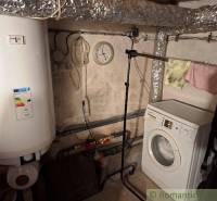 Laundry room in a family house with a washing machine, boiler, and pipes.