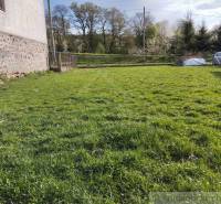 Lawn in front of the family house, parked car next to it, visible stone wall and trees.
