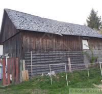 A wooden family house with a worn-out roof and fencing on a grassy plot.