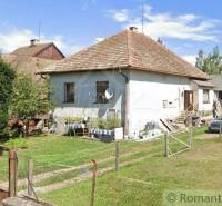 A family house with a traditional roof, a garden with greenery, next to it a farm building, a car.
