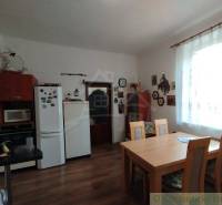 Dining room with table, chairs, and a family house with a kitchen unit, window, and decorations.