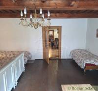 A room in a family house, wooden ceiling, chandelier, two beds, floral blankets.