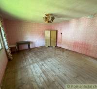 In the room of the family house, there is a table, cabinets, wooden floor, and pink wallpaper.