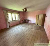 A room with a wooden floor, an antique wardrobe, pink walls, and a table in a family house.