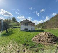 The family house stands on a green meadow, surrounded by trees and a blue sky.