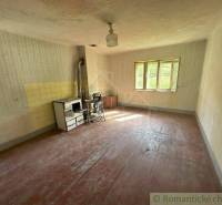 An old family house with a tiled stove, wooden floor, and light through the window.