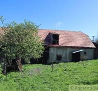 A family house with an old roof, a veranda, and a natural garden in a village setting.