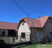 A family house with a sloped roof, an adjacent building, and a yard under the blue sky.