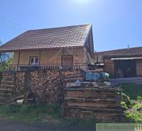A family house with trees in the yard, wooden pallets next to it, an extension in the background.