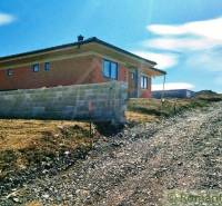 A family house on a slope next to a gravel road is surrounded by a clear blue sky.