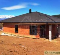 Construction of a family house with a black roof in a picturesque rural setting with mountains.