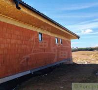 A family house under construction with a brick wall in the countryside, with nature and fields in the background.