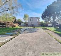 A paved plot with trees and a house in the back, suitable for recreational living.