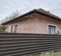 A family house with a metal fence and a satellite dish, with flower beds in the background.