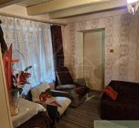 A room in a rustic cottage with a comfortable armchair, floral decorations, and wallpaper.