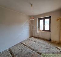 A room in a family house with an unfinished floor, one window, and a hanging light fixture.