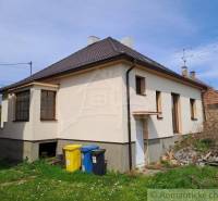 A family house with two ground-floor windows, a lawn, and waste containers in the yard.