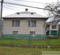 A family house with a white metal fence and green lawn, next to an old tree.