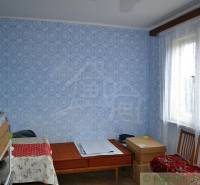 A room with patterned wallpaper, decorated in blue, next to it is a family house.
